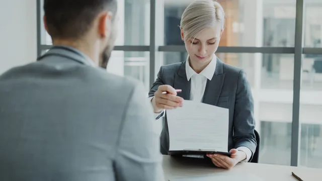 Business professionals reviewing a contract in a modern office setting. Lovpligtige og frivillige goder i ansættelsen