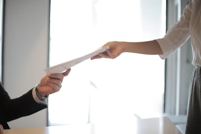 Close-up of hands exchanging documents in a business setting indoors. Opfølgning under sygefravær: Hvad må arbejdsgiver spørge om?