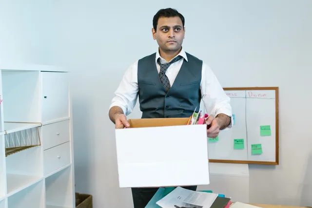 Professional man organizing office belongings in a cardboard box, preparing for transition. Opsigelsesvarsler i funktionærloven: Sådan beregnes de