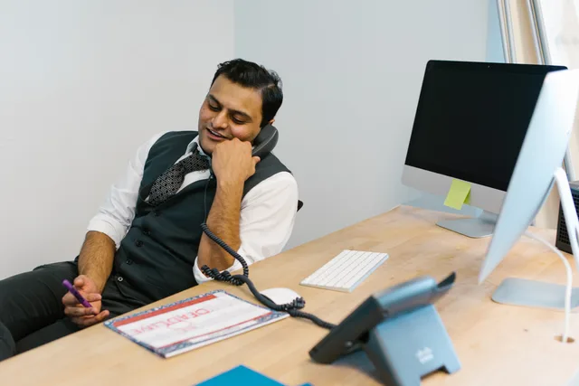 Smiling businessman engaged in a phone conversation at a modern office desk. Sådan melder du dig syg på jobbet